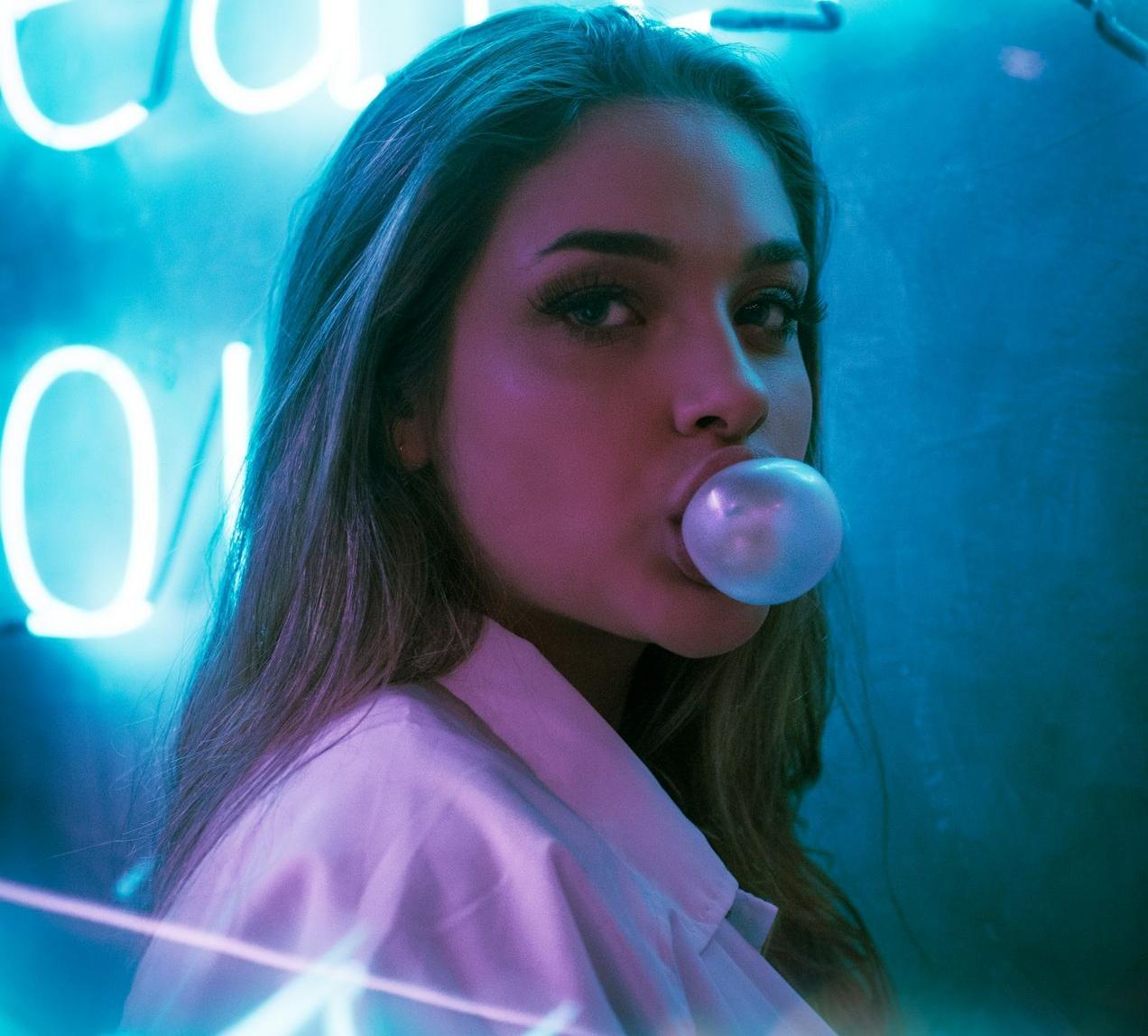 selective focus photo of woman blowing gum standing in front of turned-on neon signage